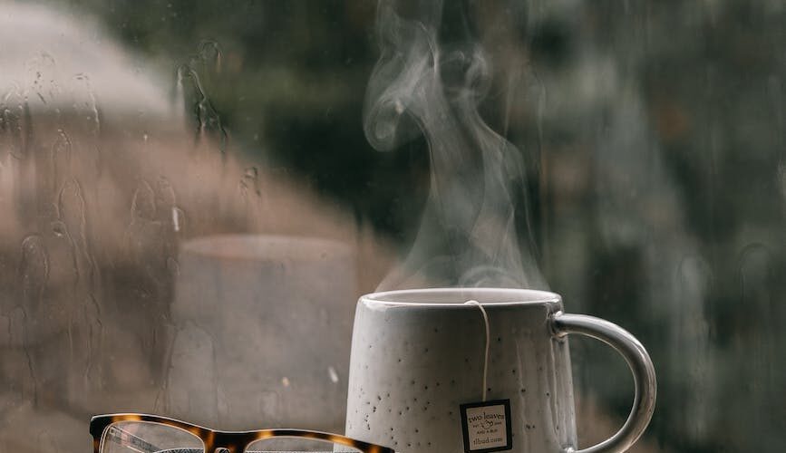 cup of tea and an eyeglasses on the stacks of books near the window